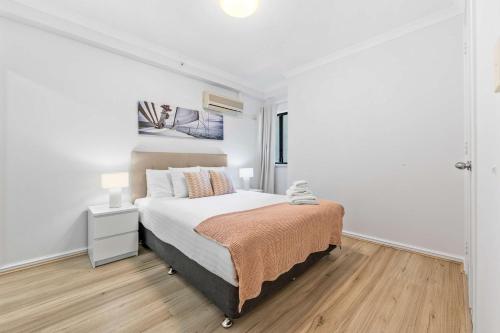 a white bedroom with a bed and a wooden floor at Convenient East Perth Stay with Free Parking in Perth
