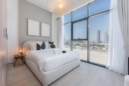 a white bedroom with a bed and a large window at Free housekeeping visits during your stay - StayShort - Modern 1-Bedroom Apartment at Azizi Riviera in Meydan in Dubai