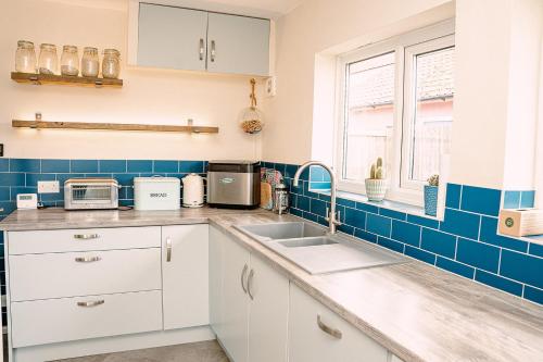 a kitchen with white cabinets and blue tiles at Pass the Keys Dungeness Drift - By the Beach in Folkestone