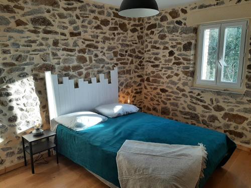 une chambre avec un lit et un mur en pierre dans l'établissement Les Carbonniers, à Saint-André-de-Najac