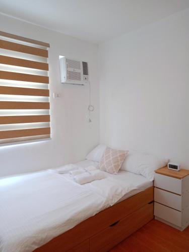a white bedroom with a bed and a window at Bali inspired 2 bedroom in Lipa netflix pool and parking in Muntingpulo