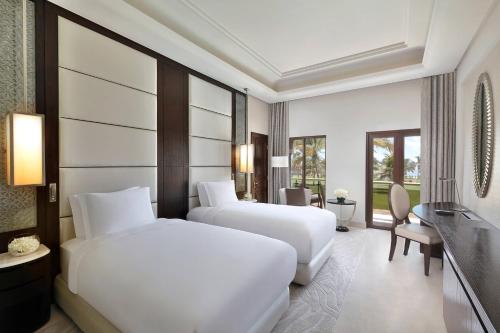 a hotel room with two beds and a desk at Al Bustan Palace, a Ritz-Carlton Hotel in Muscat