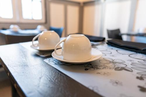 two white cups and saucers on a wooden table at De Blasis Budget Rooms in Santiago