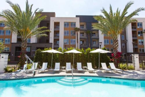 a pool with chairs and umbrellas in front of a building at 3 Miles to Disney Heated Pool CnvntnCtr Jacuzzi in Fullerton