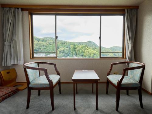 a room with two chairs and a table and a window at Shuzenji Onsen Hotel Takitei in Izu