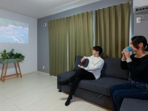 two people sitting on a couch playing a video game at ゲストハウス岐阜羽島心音 Guest House Gifuhashima COCONE in Hashima