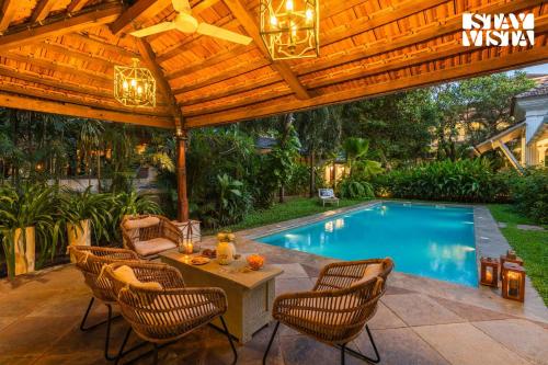 a patio with a wooden pergola and a swimming pool at StayVista at A Portuguese Tale - Pool, Bar & BBQ in Assagao