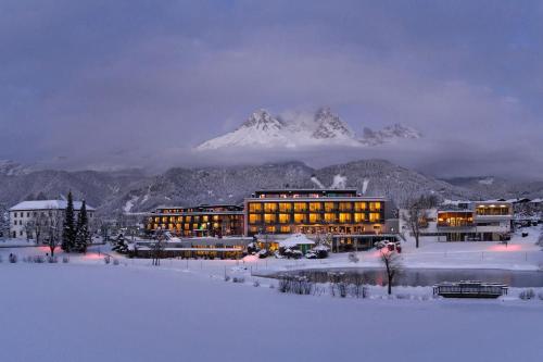 a building in the snow with a mountain in the background at Ritzenhof - Hotel und Spa am See 4-Sterne-Superior in Saalfelden am Steinernen Meer
