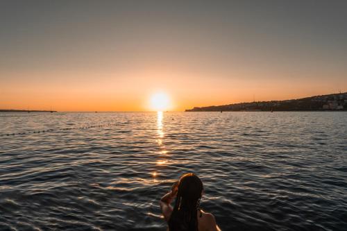 a woman sitting in the water watching the sunset at The Sea Lodges Portoroz - Hausboot Floating Sea House in Portorož