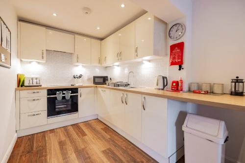 a kitchen with white cabinets and a clock on the wall at Bright House with Garden & Patio in Market Town in Inverurie