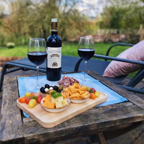 a wooden table with two glasses of wine and a plate of food at Roulotte Ravel-Emoi Chambre Insolite de Charme in Ramillies