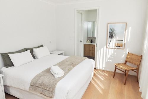a white bedroom with a large bed and a chair at The Elanora in Dunsborough
