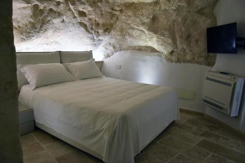 a bedroom with a white bed with a stone wall at 5 Elementi Sassi Matera in Matera