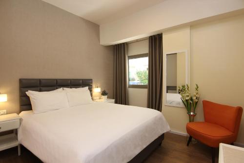 ein Schlafzimmer mit einem großen weißen Bett und einem orangenen Stuhl in der Unterkunft Idelson Hotel in Tel Aviv