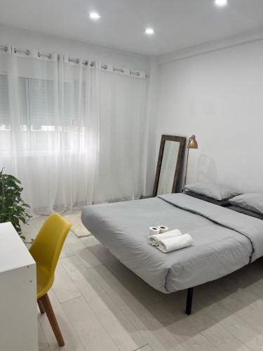 a white bedroom with a bed and a yellow chair at Orquídea in Cacém