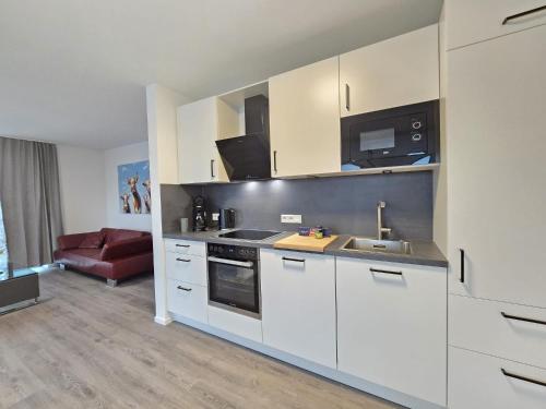 a kitchen with white cabinets and a red couch at Ferienwohnung NorderHafen in Norden
