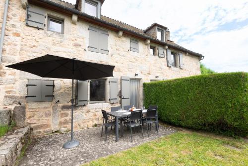 a table and chairs with an umbrella in front of a building at Gîte Gîtes de France 4/6 personnes A in La Fage-Saint-Julien