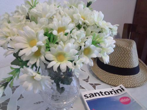 a vase filled with white flowers next to a hat at Kiklamino Sunset Studios in Oia