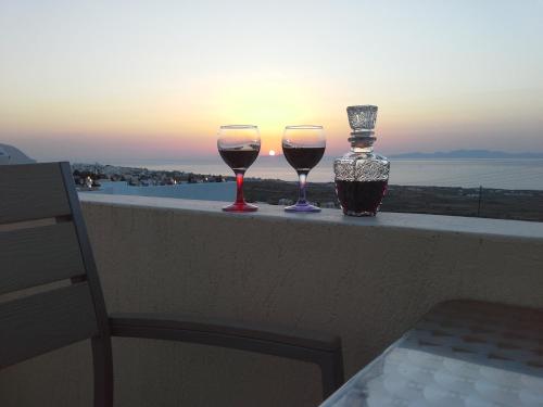 two glasses of wine sitting on a ledge with the sunset at Kiklamino Sunset Studios in Oia