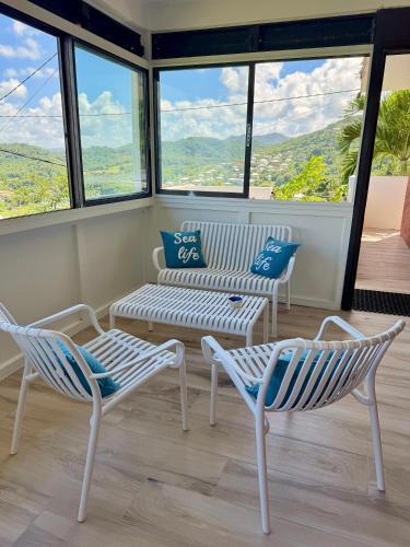 a room with two chairs and a bench and windows at La villa Azur classée 3 étoiles Moderne et Confortable à deux pas de la plage de l Anse à l Ane Trois Îlets - Services Petit Dej sur demande in Les Trois-Îlets