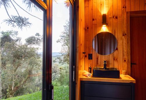 a bathroom with a mirror and a sink and a window at Cabana na Serra Lareira e Vista Deslumbrante in Rio Rufino