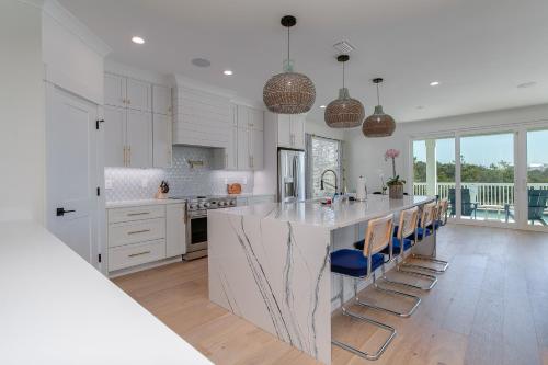 a white kitchen with a large island with blue bar stools at LUXE Azul Oasis PRIVATE Pool Views Walk to Beach Pets Sleeps 14 in Orange Beach
