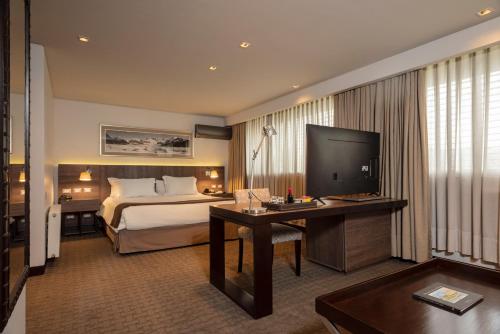 a hotel room with a bed and a desk and a television at Hotel Los Españoles Plus in Santiago