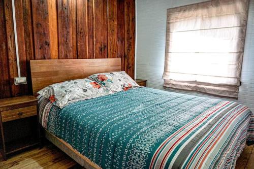 a bedroom with a bed with a blue comforter and a window at Cabaña La Granja de Tía Cone, Llanada Grande in Llanada Grande