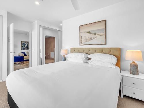 a white bedroom with a large white bed with two lamps at 3-Bed: Riverfront Alfresco Dining & Rooftop Pool in Batemans Bay