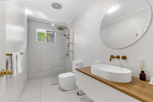 a bathroom with a sink and a toilet and a mirror at Cedar Villa - A Designer Pool House by the Beach in Palm Cove