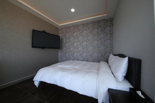 a bedroom with a white bed with a tv on the wall at Hotel memory Jumunjin- Welcome drink provided in Gangneung