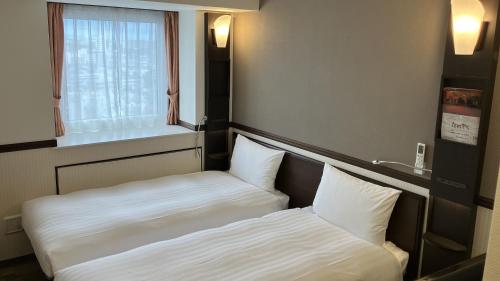 two beds in a small room with a window at Toyoko Inn Nishi-kawaguchi-eki in Warabi