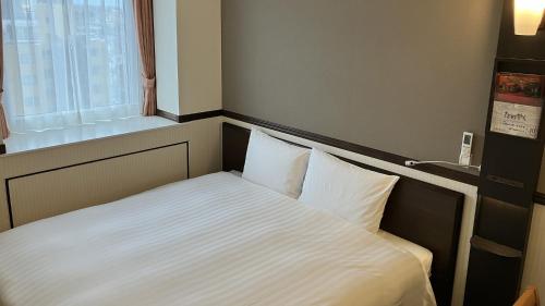 a bed in a small room with a window at Toyoko Inn Nishi-kawaguchi-eki in Warabi