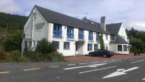 a white building with blue windows and a car parked in front at Lochgair Hotel in Lochgair