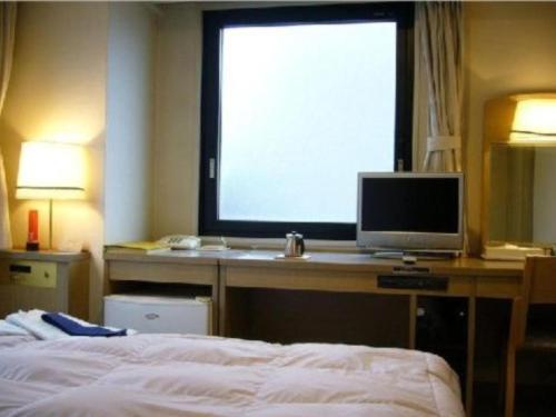 a bedroom with a bed and a computer monitor on a desk at Silk Hotel in Ichinomiya
