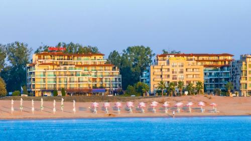 a group of pink umbrellas on a beach with buildings at Aparthotel Hotel Prestige City II in Primorsko
