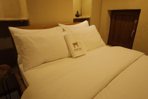a bed with white sheets and pillows in a room at بيت الصباح نزل وكافيه Bait AlSabah Heritage Inn & Cafe in Birkat al Mawz