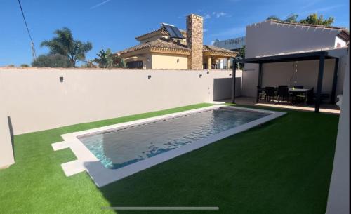 un patio trasero con piscina y césped verde en Villa Bolet, en Chiclana de la Frontera