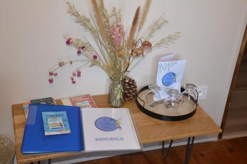 a table with a vase of flowers and a book at Le colibri bleu in Argeliers