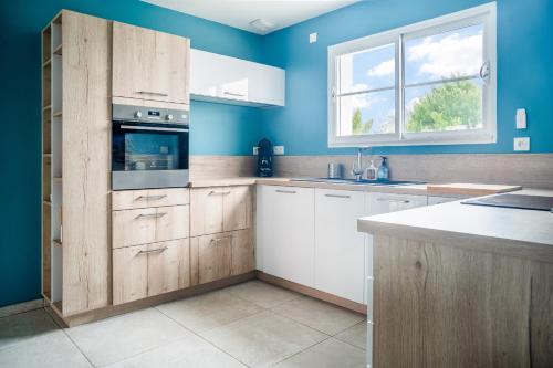 une cuisine avec des placards en bois et un mur bleu dans l'établissement Grande maison moderne pour 6, à Saint-Vincent-sur-Jard