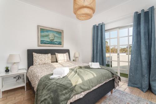 a bedroom with a bed with blue curtains and a window at Host Wise - Quiet Spacious House - Swimming Pool in Benagil