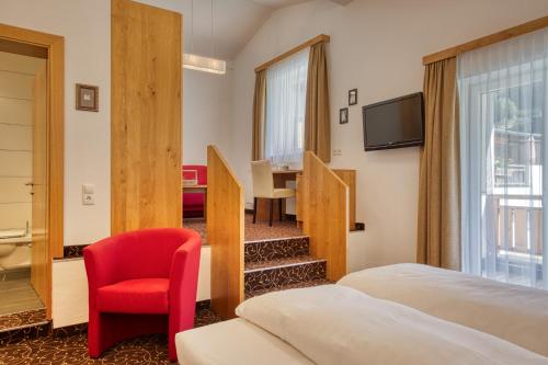 a hotel room with two beds and a red chair at Hotel Erika in Nauders