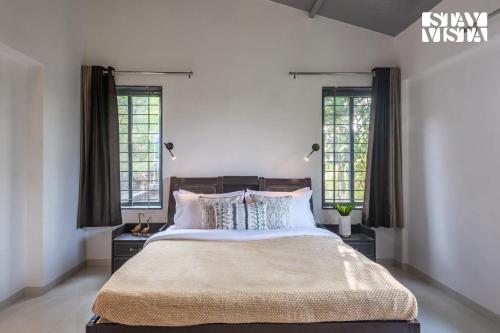ナーシクにあるStayVista at Banyan Nirvana Villa with Pool, Bonfire & Lawnの大きなベッドと2つの窓がある寝室