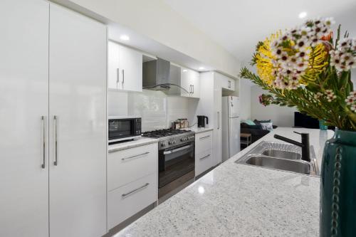 a white kitchen with white cabinets and a sink at Jetty Road Holidays - 33 Jetty Road in Normanville