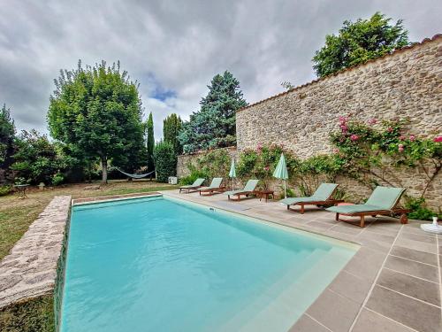 - une piscine avec des chaises longues et des chaises à côté d'un mur en pierre dans l'établissement Le relai des Artistes, à Bessines-sur-Gartempe