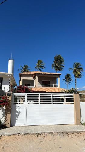 a white fence in front of a house with palm trees at Casa Atlantico Flecheiras in Trairi