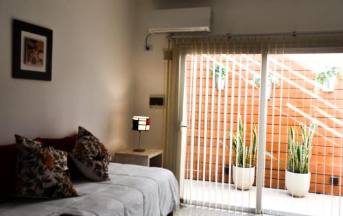 ein Schlafzimmer mit einem Bett und einem Fenster mit Topfpflanzen in der Unterkunft Villa María Urban Aparts in Villa María