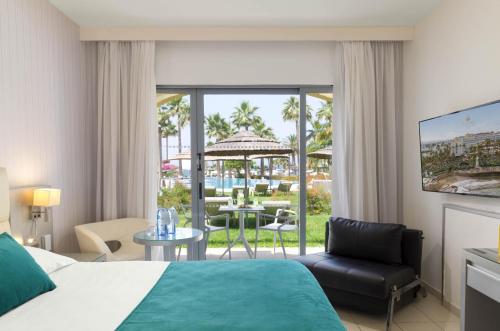 a hotel room with a bed and a view of a patio at St George Beach Hotel & Spa Resort in Paphos City