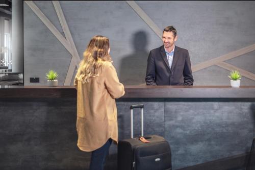 a man and a woman standing at a counter with a suitcase at Garner Hotel Augsburg Nord by IHG in Augsburg
