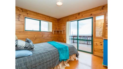 a bedroom with wooden walls and a bed with a large window at Wine Downtime - Mangawhai Holiday Home in Mangawhai